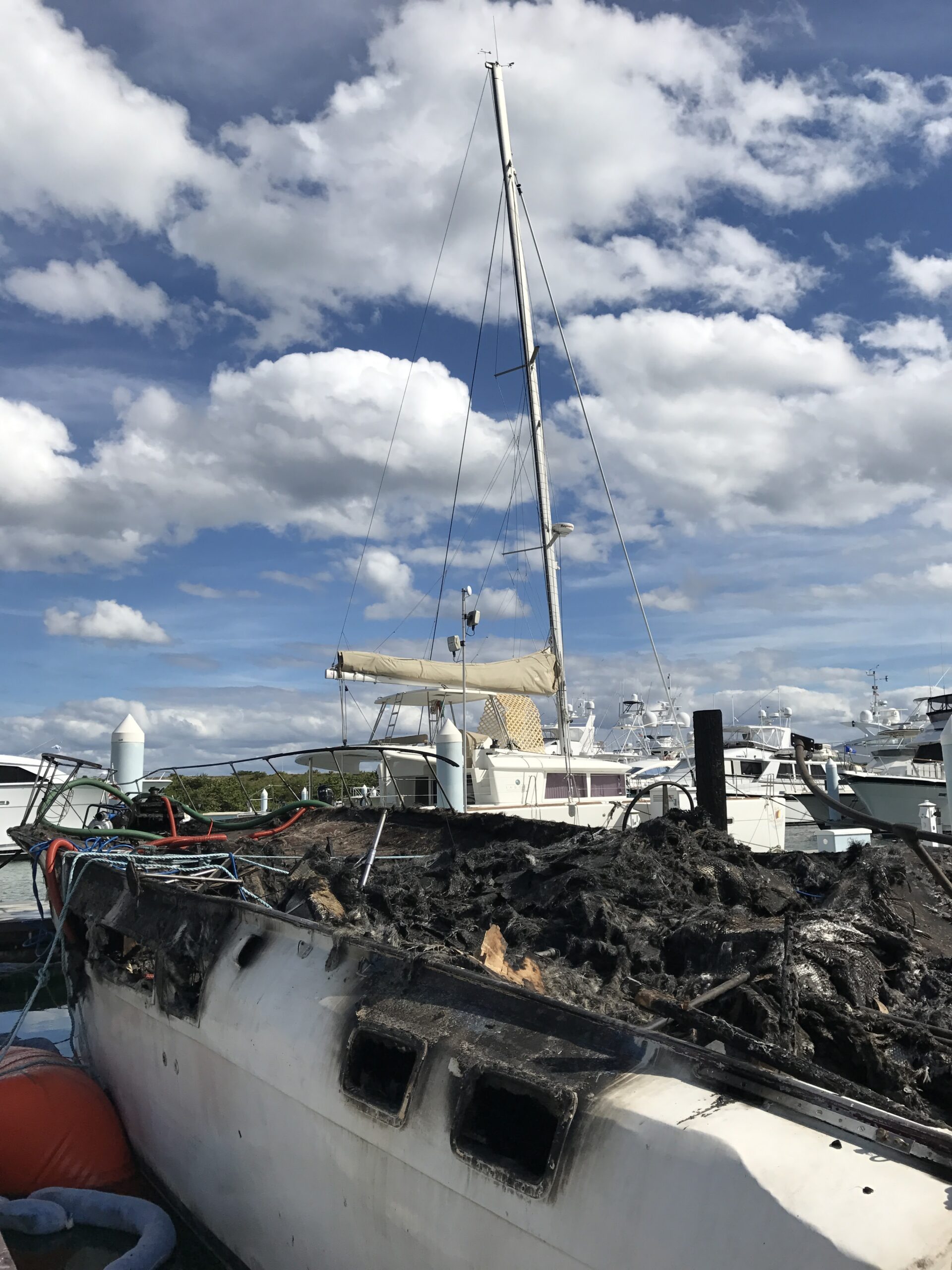 The shell of a boat which burned to the waterline sits in the foreground while the s/v Dawn Treader (a Lagoon 450 catamaran) is visible in the background.